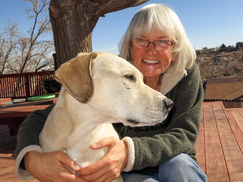 Mom embracing Roxy on a sunny wooden deck.